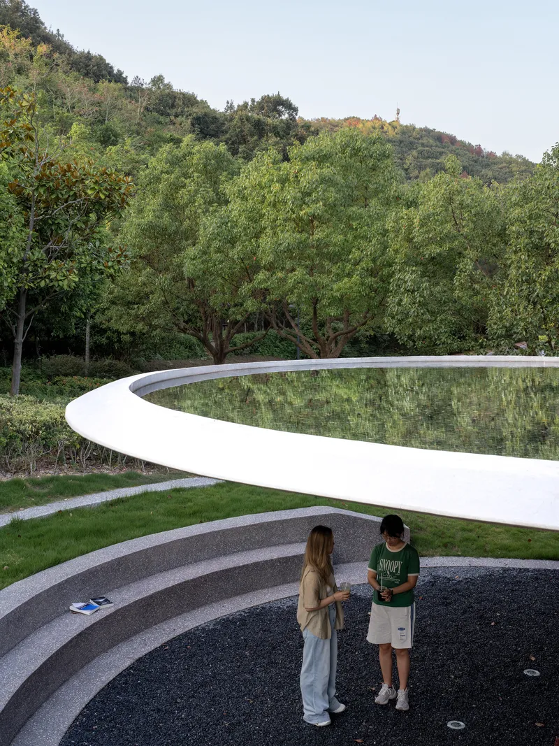 Curved white parapet edge beside reflecting pool with two visitors on terraced steps at dusk