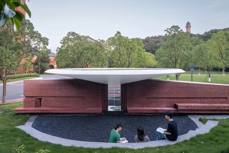 Pavilion with thin white canopy sheltering brick walls and a sunken courtyard where students sit reading