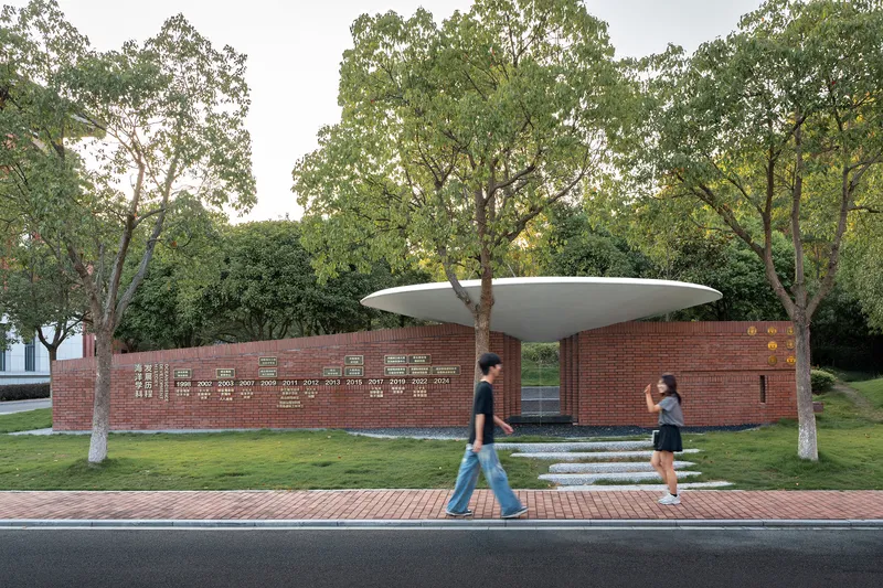 Street view of the brick memorial wall with inscribed names beneath the canopy and pedestrians passing