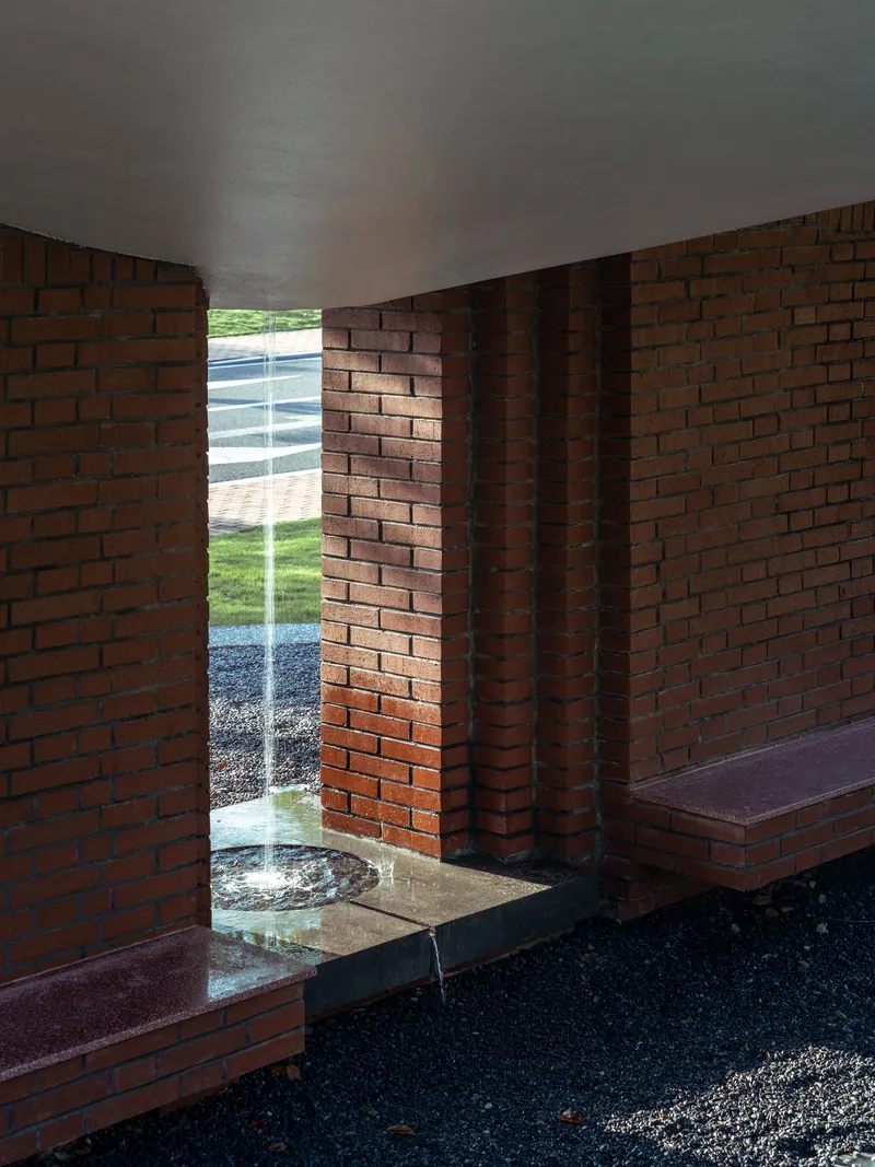 Interior view through the narrow brick opening with built-in benches and water feature beyond