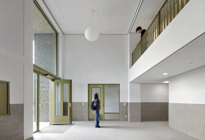 Double-height entrance lobby with terrazzo wainscoting, green metal door frames, and a mezzanine above