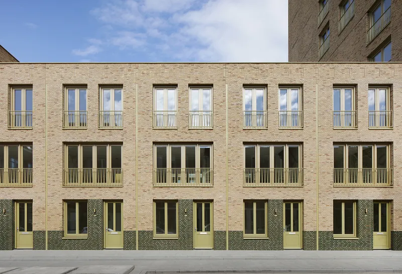 Symmetrical courtyard facade with alternating window heights and pale green balcony railings in buff brick
