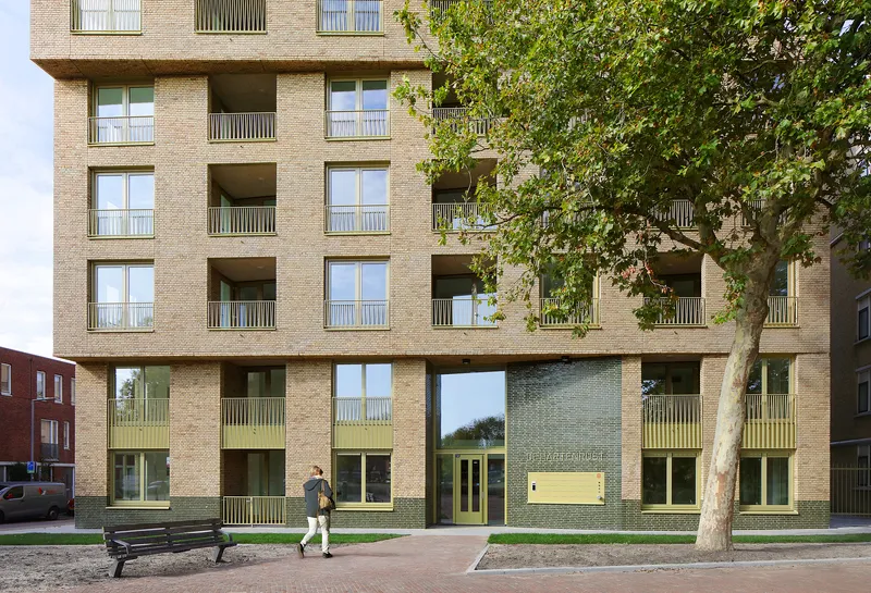 Ground-level facade showing recessed balconies with metal railings and a pedestrian walking past a bench