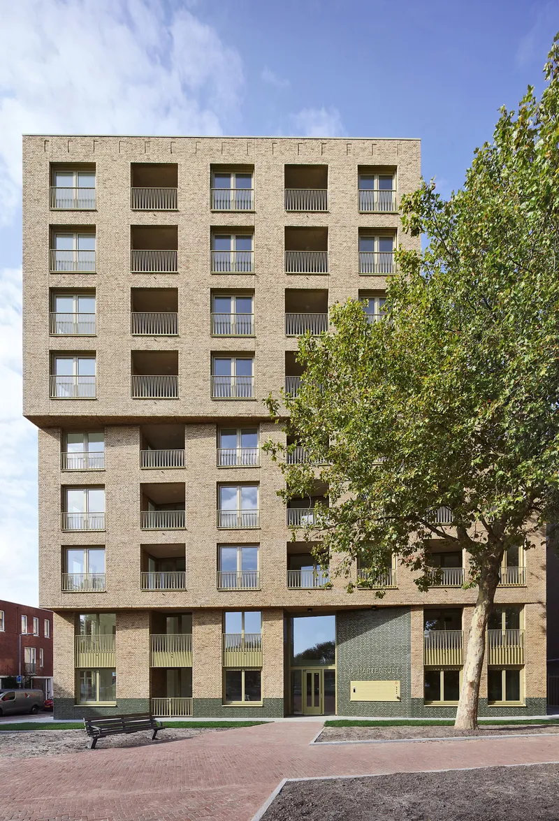 Ground floor entry with pale green panels beneath recessed balconies and a street tree