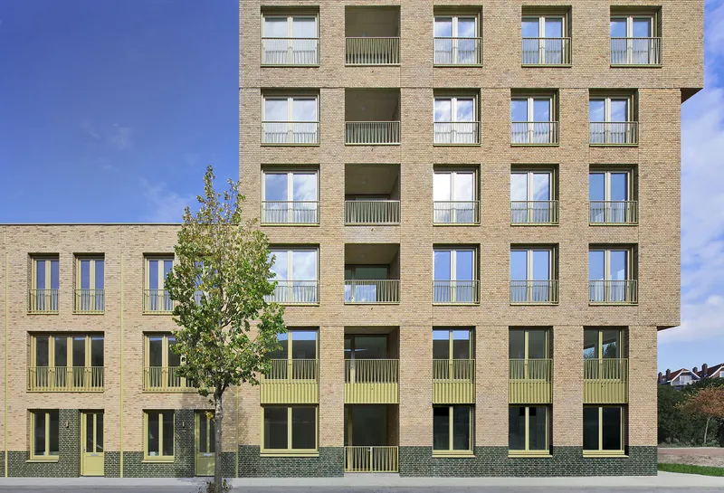 Front elevation with a young street tree against the buff brick and recessed balcony grid