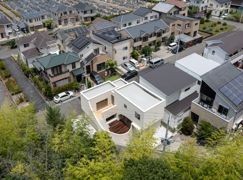 Aerial view of white rooftop with curved courtyard and timber deck nestled within a dense suburban neighborhood