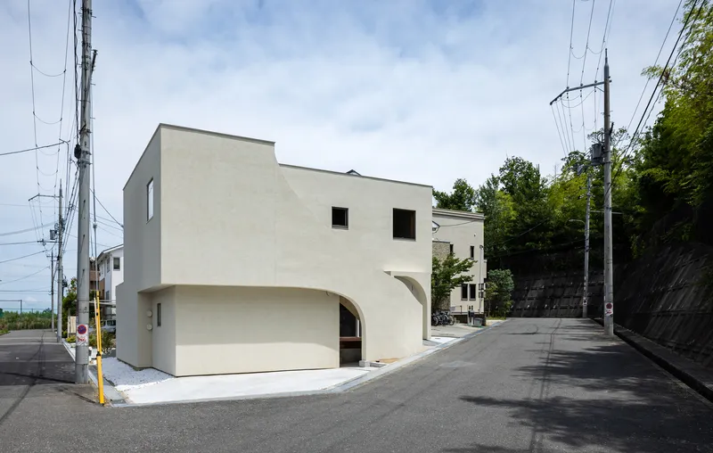 Corner facade with arched recesses at the base and punched square windows above on a sloped street