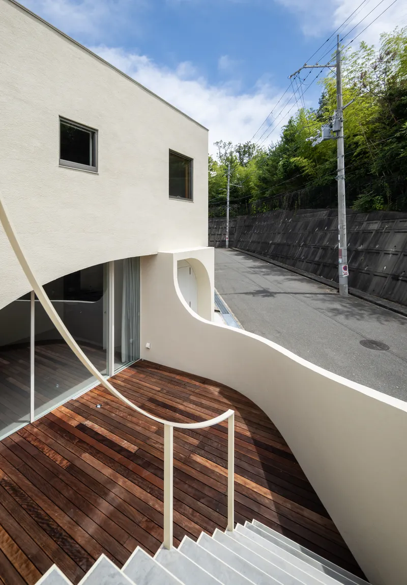 Curved timber deck terrace with white metal railing descending into a sunken outdoor space below a clear sky