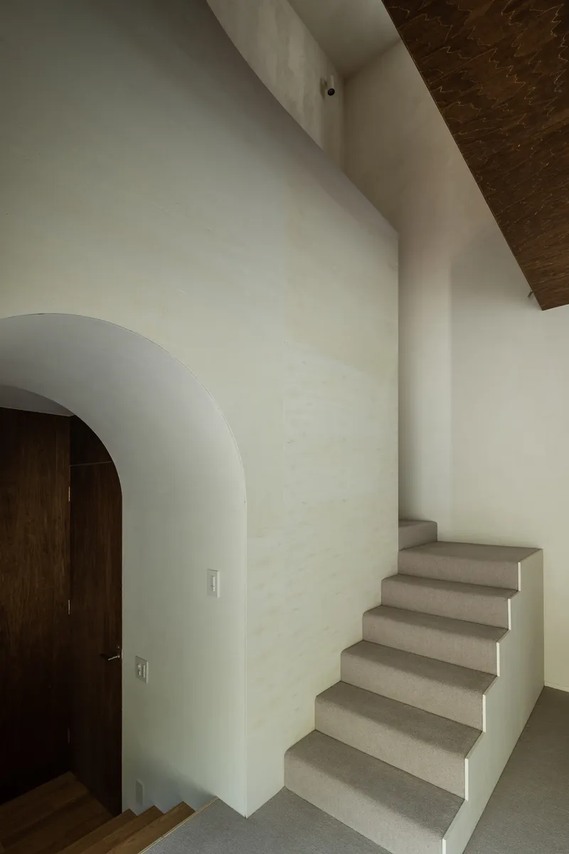 Interior staircase with pale terrazzo treads rising alongside a white wall with an arched doorway and timber ceiling