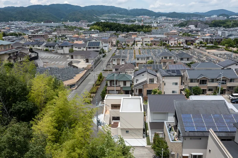 Elevated view of rooftop courtyard opening within residential blocks backed by forested mountains under cloudy skies
