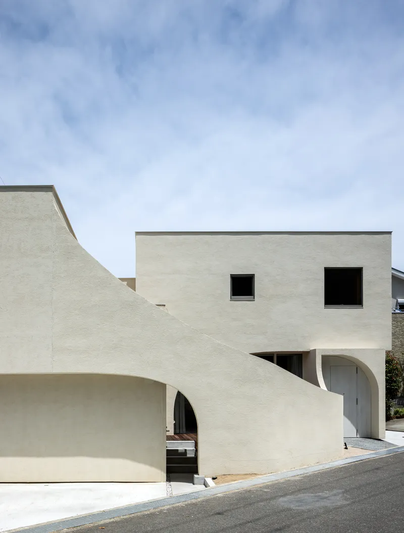 Street view of pale stucco facade with curved walls and arched openings under blue sky
