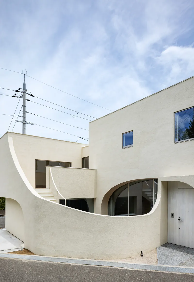 Curving exterior staircase rising between stucco volumes with utility wires crossing overhead