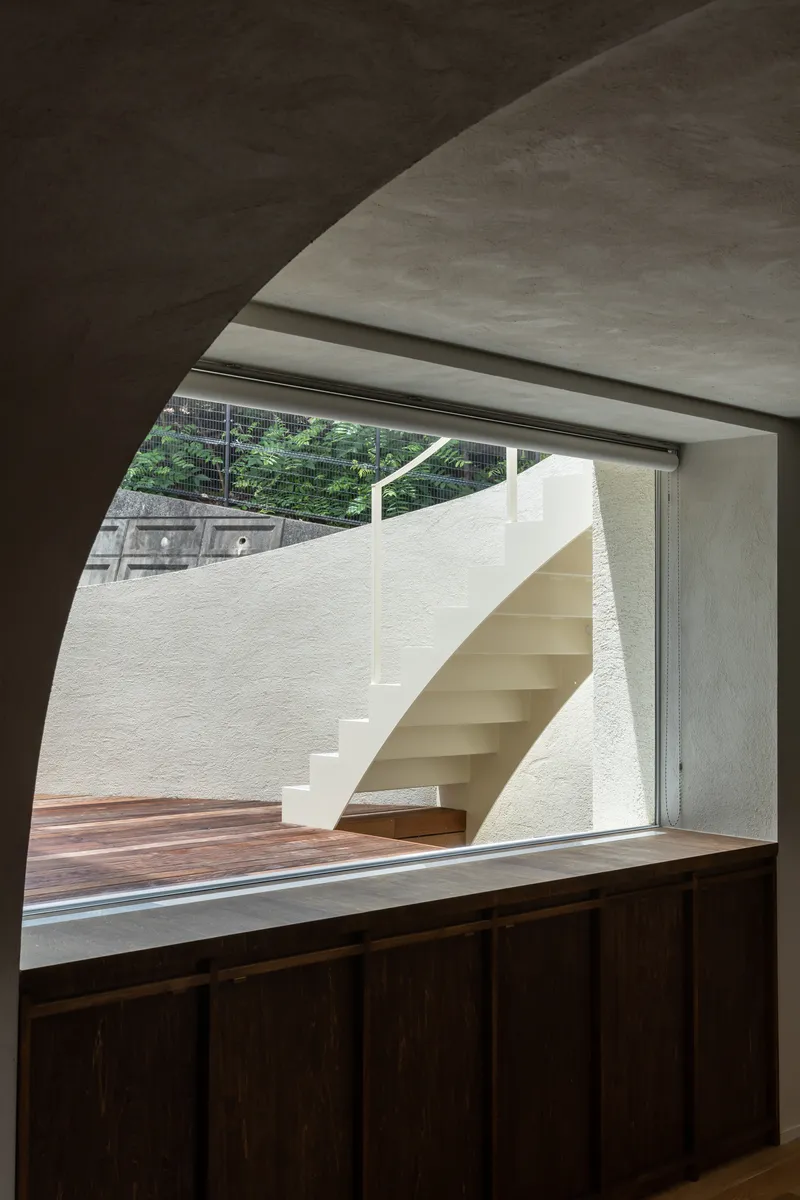 Interior view through arched opening to exterior staircase and planted hillside beyond