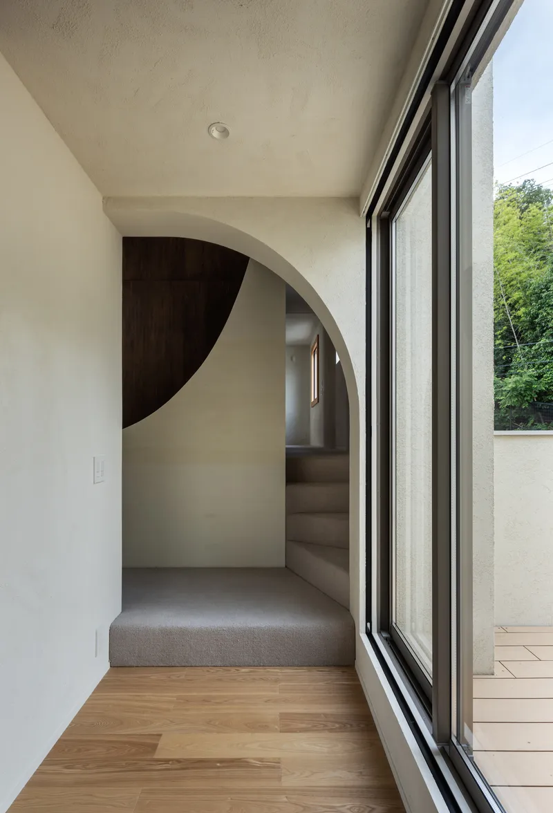 Interior view of arched stair passage beside floor-to-ceiling glazing overlooking green foliage
