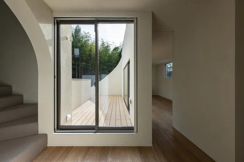 Glass door opening to timber deck terrace framed by white walls and trees beyond