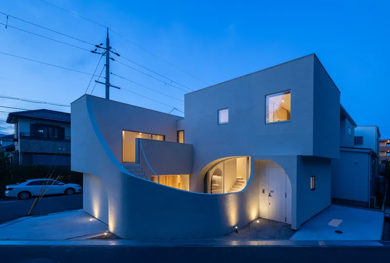 Street view of the grey facade with curved openings and uplighting at blue hour