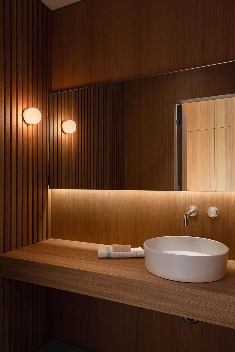 Bathroom vanity with timber slat wall, backlit mirror and two spherical wall sconces