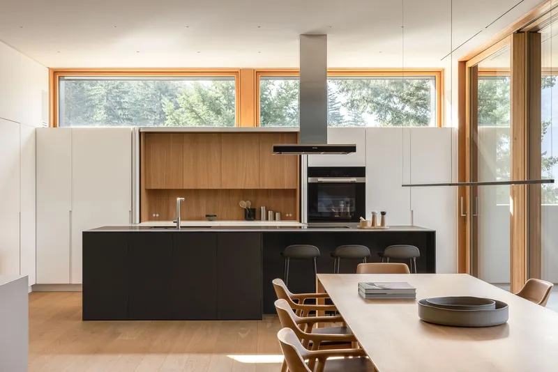 Kitchen with black island, timber backsplash and horizontal strip windows framing trees outside
