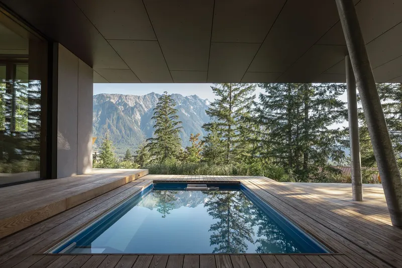 Covered timber deck with sunken pool framing a view of forested mountains beyond steel columns