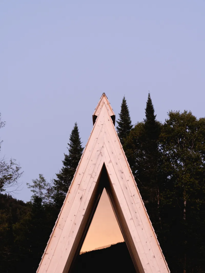 Tall triangular timber frame portal set against dusk sky and darkening conifer treeline