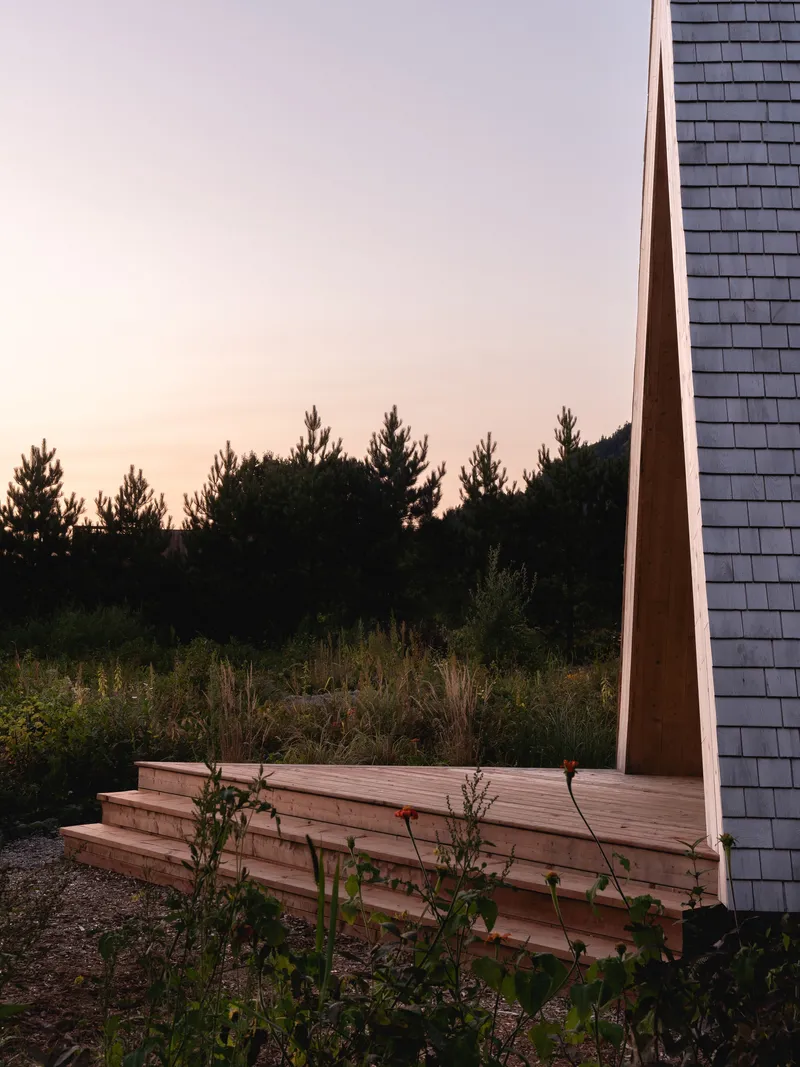 Timber bench and entry steps beneath angled frame with shingle wall at sunset