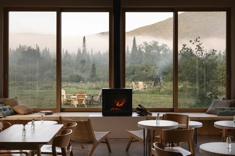 Central woodstove and floor-to-ceiling windows overlooking meadow and forested hills shrouded in morning mist