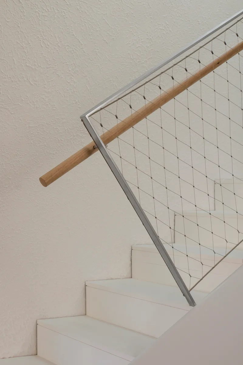 White stair with timber handrail and steel mesh balustrade against a textured plaster wall