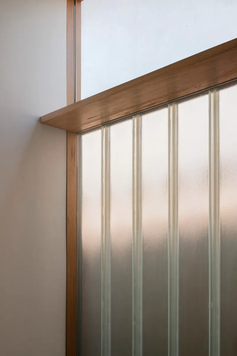 Close-up of timber handrail meeting translucent polycarbonate wall panel with vertical supports