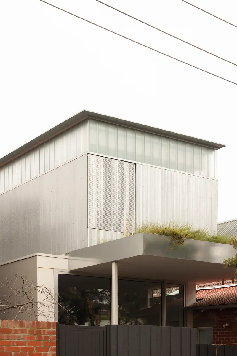 Close view of the weathered metal cladding and planted terrace beneath a pale overcast sky