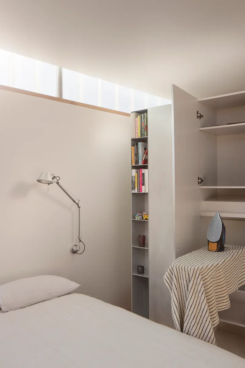 Bedroom with high clerestory windows above built-in bookshelf and articulated wall lamp