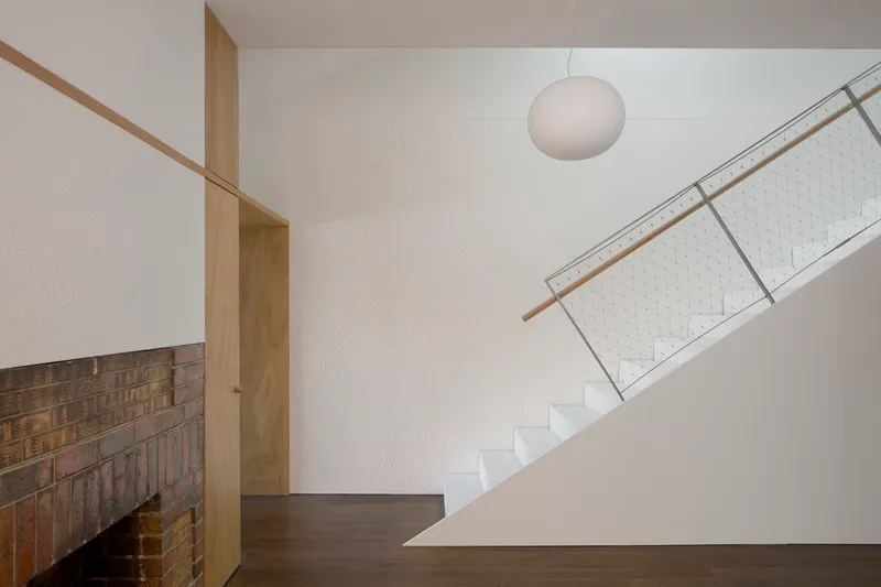 Staircase with timber handrail and wire mesh balustrade beside a textured brick wall
