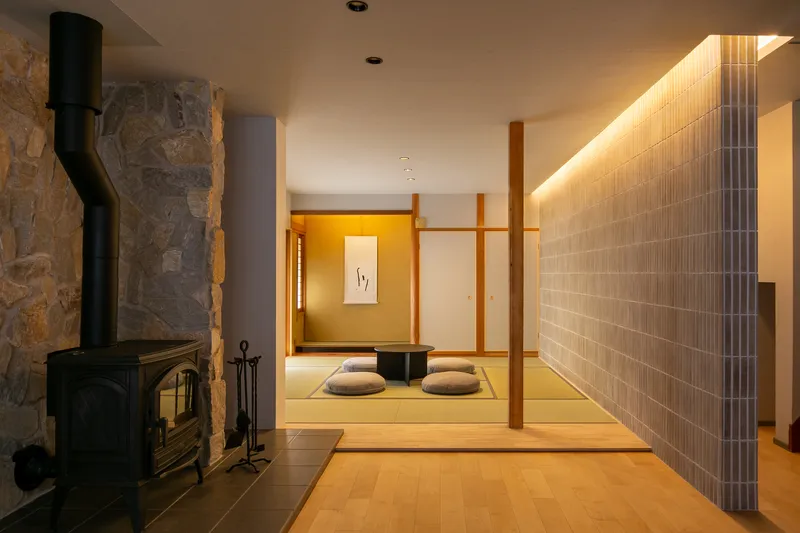 View through living space to tatami room with floor cushions, stone fireplace and backlit grey tile wall