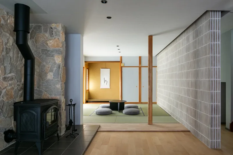 Black woodstove against a fieldstone wall beside a tatami room with vertical slatted screen