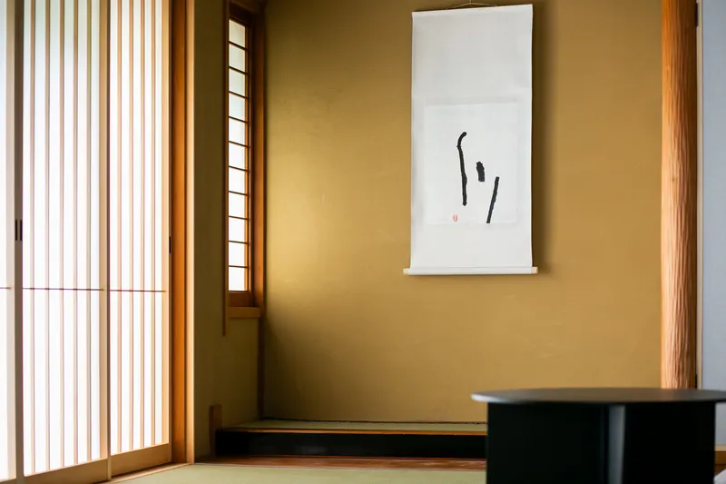 Tatami alcove with scroll painting on ochre wall beside vertical slatted screen in warm daylight