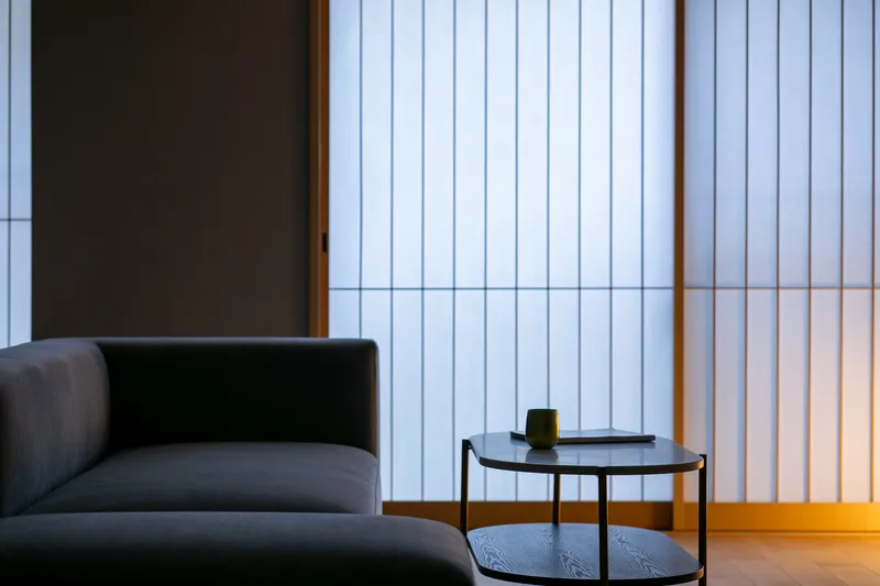 Side table and sofa against translucent vertical slat screens with timber frames at dusk