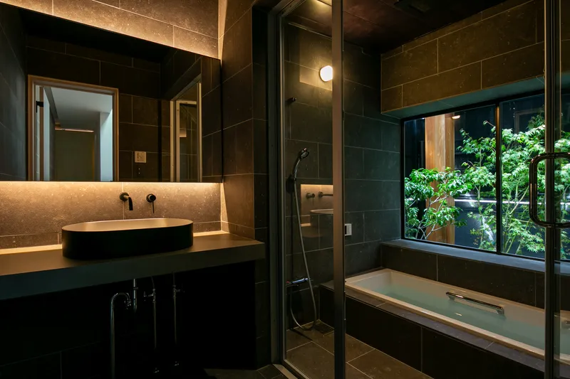 Bathroom with vessel sink and soaking tub facing window view of planted courtyard at night
