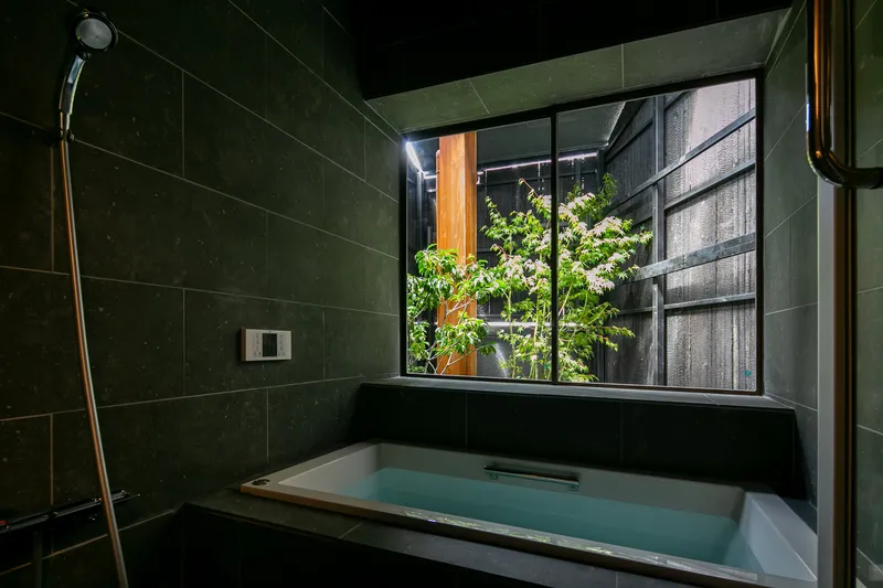 Tiled bath with recessed tub looking through window to planted courtyard at night