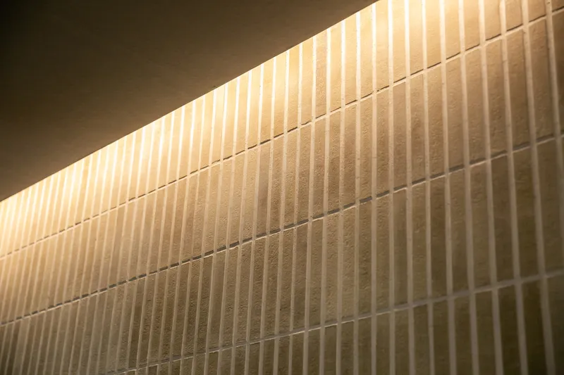 Close-up of backlit vertical ribbed tile wall with concealed linear lighting above