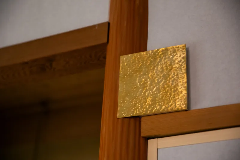 Detail of hammered brass plate inset into the timber doorframe corner joint