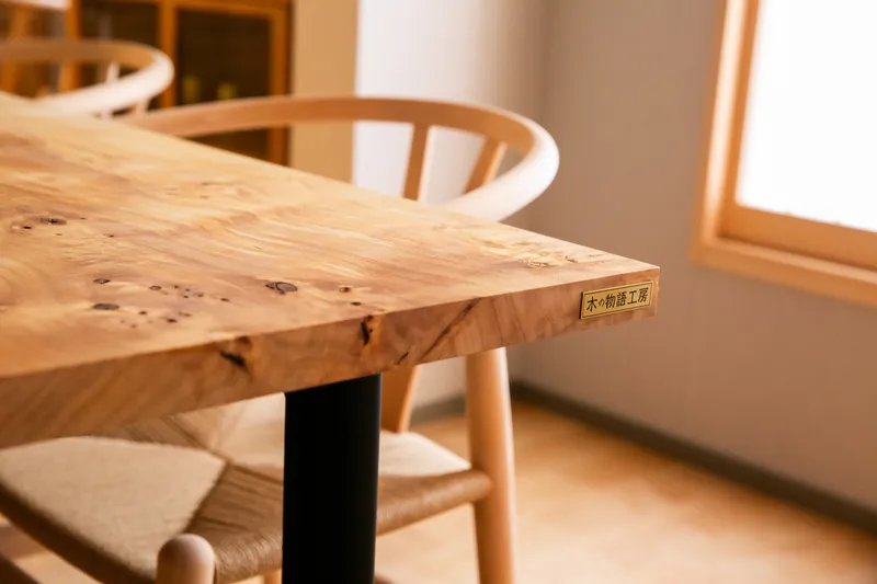 Close view of live edge timber table corner with black steel leg and woven chair seats in afternoon light