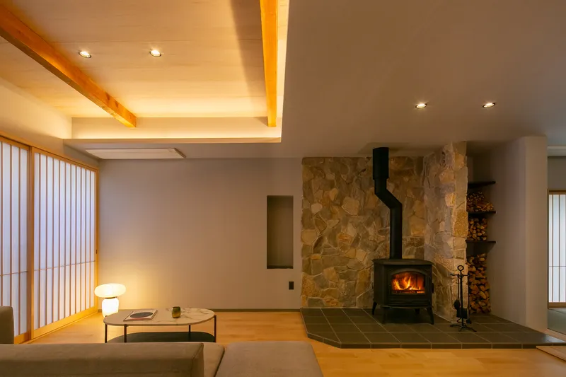 Living room with black wood stove against stone wall, recessed ceiling cove lighting and vertical timber screens