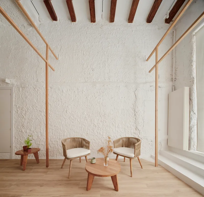 Seating area beneath exposed timber ceiling beams with textured white plaster walls and a tall window