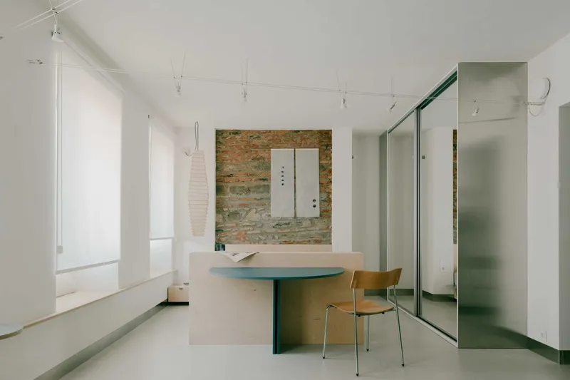 Open living space with exposed brick wall, plywood dining table and sliding glass partition under track lighting