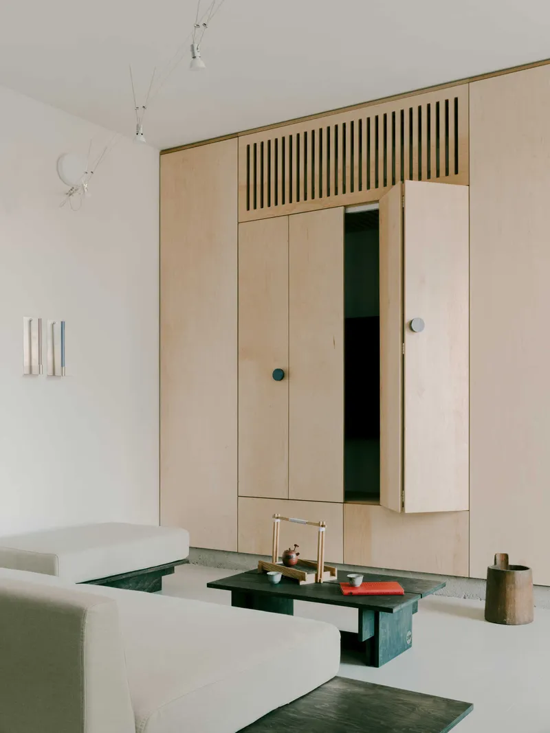Built-in plywood storage wall with vertical slatted ventilation panel above hinged cabinet doors