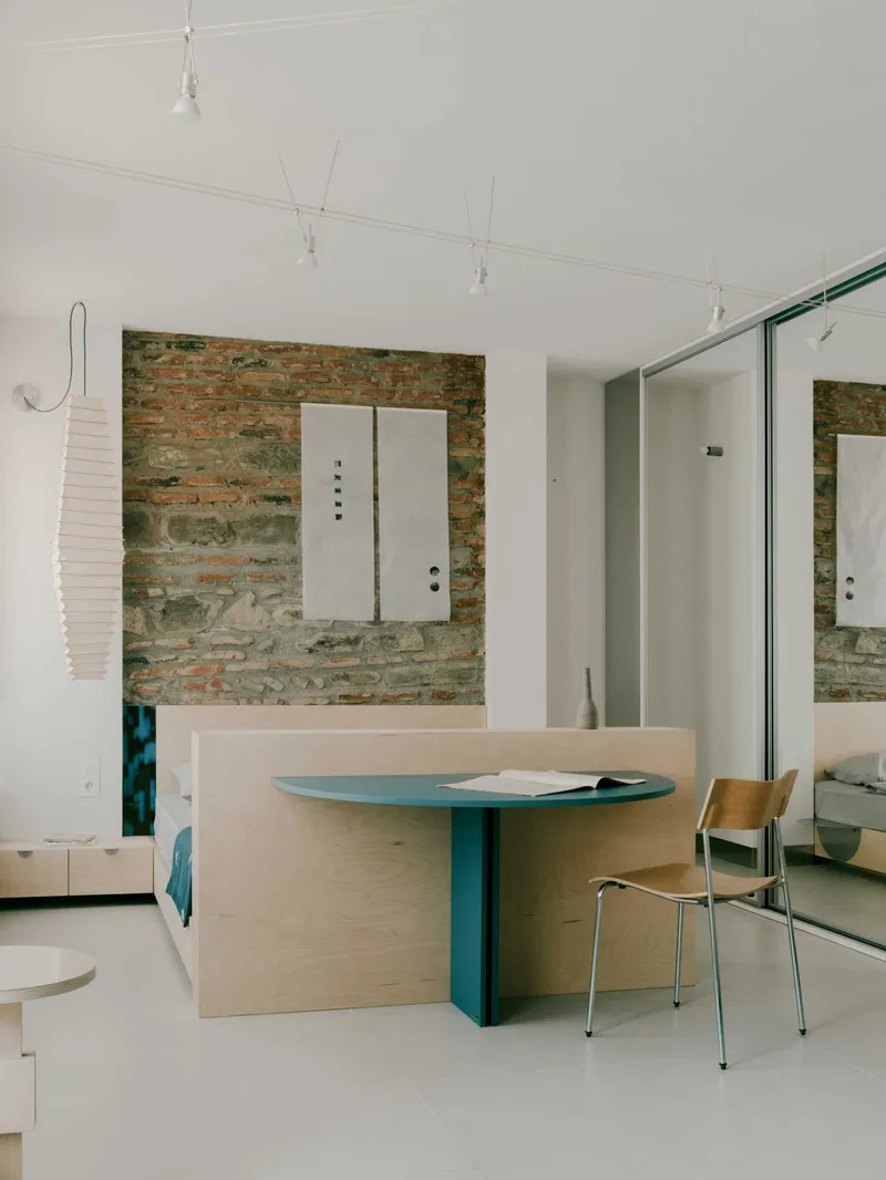 Plywood workspace with green-painted table base and mirrored wardrobe reflecting the exposed brick wall behind
