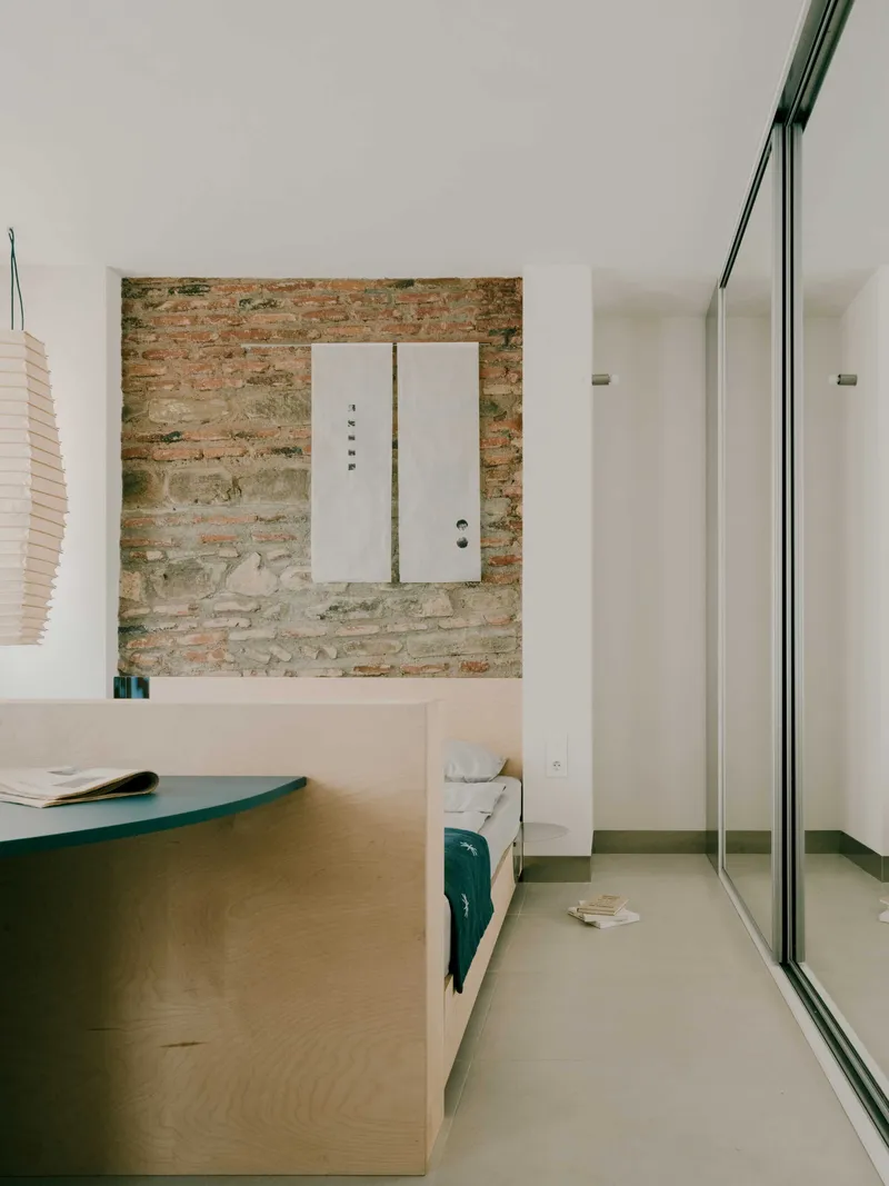 Interior bedroom with exposed brick wall, white security door, and full-height glazing on the right