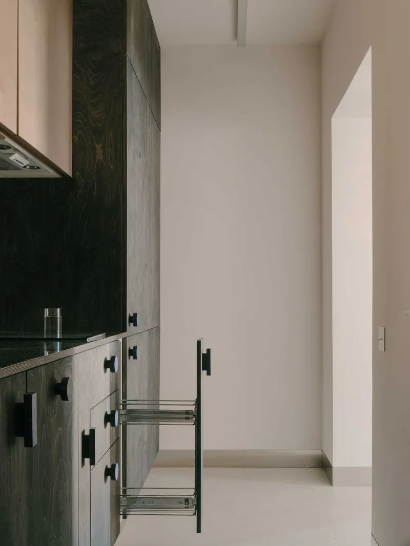 Narrow kitchen with dark wood base cabinets, black bar pulls, and open pull-out wire storage basket