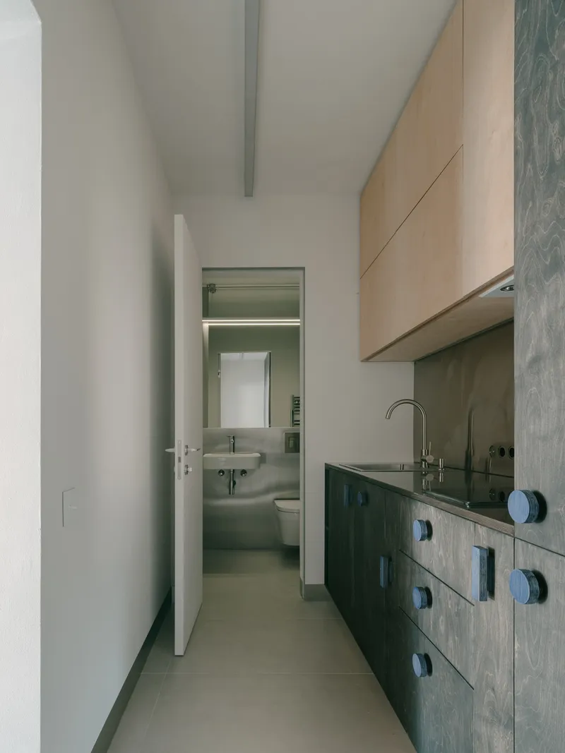 Kitchen corridor looking toward bathroom with sink visible through open door and exposed ceiling beam above