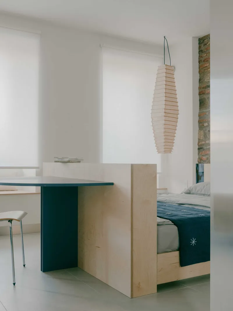 Plywood sleeping platform with green base and paper lantern pendant in a white interior