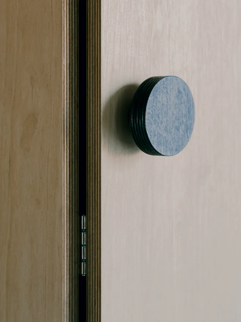 Close-up of a circular blue-grey door knob mounted on a light wood door with exposed plywood edge